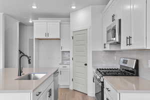 Kitchen with stainless steel appliances, white cabinets, light stone counters, a kitchen island with sink, and recessed lighting