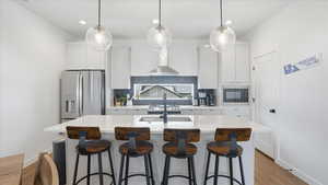 Kitchen featuring a kitchen bar, stainless steel fridge, white cabinetry, an island with sink, and backsplash