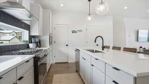 Kitchen with appliances with stainless steel finishes, wall chimney exhaust hood, white cabinetry, decorative light fixtures, and a breakfast bar