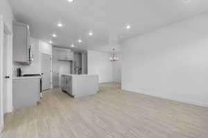 Kitchen featuring a kitchen island with sink, gray cabinetry, gas range, a chandelier, and light wood finished floors