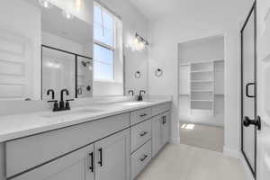 Bathroom featuring a shower stall, double vanity, a spacious closet, and light colored carpet