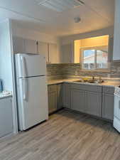 Kitchen featuring gray cabinetry, white appliances, tasteful backsplash, light wood-style flooring, and light countertops