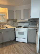 Kitchen featuring gray cabinets, white gas range oven, light countertops, light wood finished floors, and backsplash