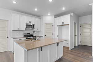 Kitchen featuring dark wood-style floors, white cabinetry, appliances with stainless steel finishes, a center island with sink, and recessed lighting