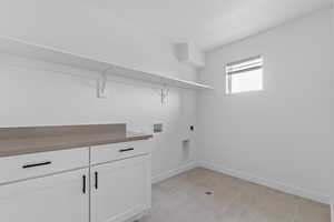 Laundry area featuring hookup for a washing machine, hookup for an electric dryer, cabinet space, and light tile patterned flooring