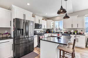 Kitchen featuring black stainless steel appliances, granite counters, LVT flooring, white cabinets, and recessed lighting