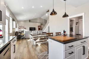 Kitchen with white cabinetry, dark solid surface quartz countertops, open floor plan, natural light, vaulted ceilings