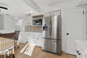Kitchen with stainless steel refrigerator with ice dispenser, light tile patterned flooring, white cabinetry, light quartz countertops, and open shelves