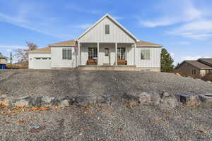 Modern inspired farmhouse featuring board and batten siding, a shingled roof, a porch, an attached garage, and gravel driveway