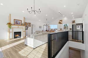 Living room with a chandelier, a glass covered fireplace, wood finished floors, high vaulted ceiling, and recessed lighting