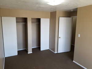 Unfurnished bedroom featuring multiple closets, dark colored carpet, and a textured ceiling