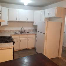 Kitchen with freestanding refrigerator, light countertops, dark wood-style flooring, gas stove, and white cabinetry