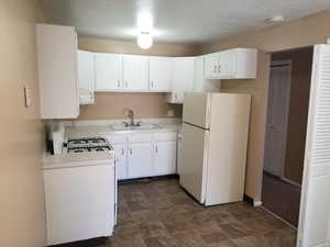 Kitchen with light countertops, white appliances, white cabinets, stone finish flooring, and a textured ceiling