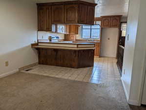 Kitchen featuring a peninsula, light tile patterned floors, electric range, light colored carpet, and a textured ceiling