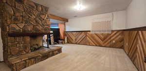 Unfurnished living room featuring wood walls, carpet floors, a wainscoted wall, a stone fireplace, and a textured ceiling