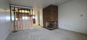 Unfurnished living room featuring a brick fireplace, light colored carpet, and a textured ceiling