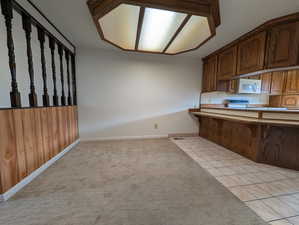 Kitchen with a kitchen bar, light tile patterned flooring, white microwave, a peninsula, and brown cabinetry