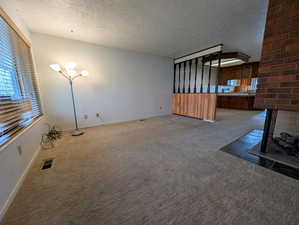 Unfurnished living room featuring a textured ceiling, carpet floors, and a fireplace