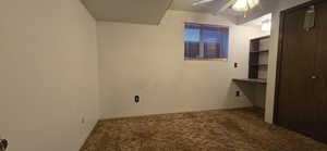 Empty room with built in study area, a ceiling fan, and carpet flooring