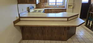 Kitchen featuring light tile patterned flooring, light countertops, a peninsula, and white appliances