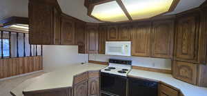 Kitchen with range with electric stovetop, light countertops, black dishwasher, white microwave, and light carpet