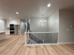 Hallway with an upstairs landing, recessed lighting, light wood-type flooring, and a chandelier