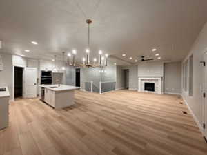 Kitchen featuring open floor plan, light countertops, a fireplace, a kitchen island with sink, and recessed lighting