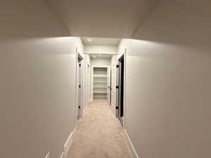 Hallway featuring light colored carpet and baseboards