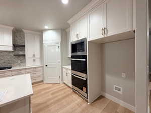 Kitchen with light wood-style floors, white cabinets, appliances with stainless steel finishes, decorative backsplash, and open shelves