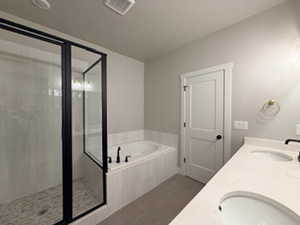 Full bathroom featuring double vanity, a bath, a stall shower, and dark tile patterned floors