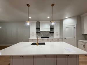 Kitchen with tasteful backsplash, white cabinets, decorative light fixtures, a kitchen island with sink, and recessed lighting