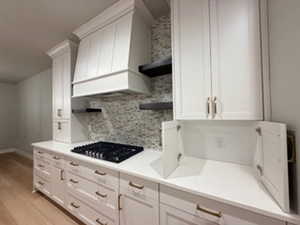 Kitchen with open shelves, white cabinets, custom exhaust hood, and light countertops