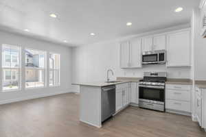 Kitchen with appliances with stainless steel finishes, a peninsula, white cabinets, recessed lighting, and light wood-style flooring