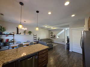 Kitchen with stainless steel appliances, light stone countertops, dark brown cabinets, hanging light fixtures, and dark wood-type flooring