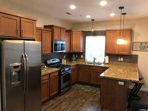 Kitchen featuring stainless steel appliances, brown cabinets, a peninsula, a breakfast bar area, and hanging light fixtures