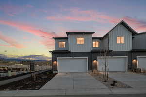 View of front facade featuring board and batten siding, driveway, an attached garage, and brick siding