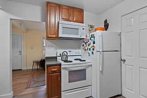 Kitchen with white appliances, brown cabinetry, and dark wood-type flooring