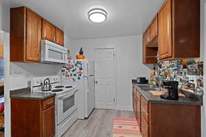 Kitchen with dark countertops, white appliances, brown cabinetry, and light wood-style floors