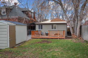 Back of house featuring a deck, a fenced backyard, a chimney, a shingled roof, and a storage unit