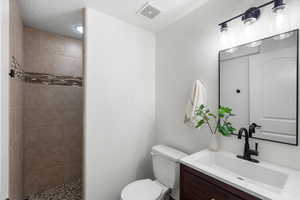 Full bathroom featuring vanity, a textured ceiling, and tiled shower