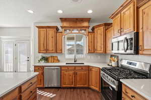 Kitchen with stainless steel appliances, dark wood finished floors, brown cabinetry, recessed lighting, and light stone counters
