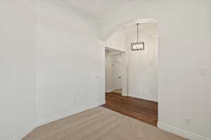Spare room featuring arched walkways, dark colored carpet, a chandelier, and crown molding