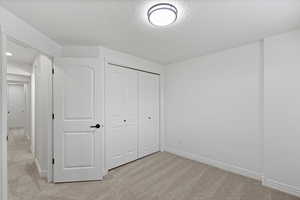 Unfurnished bedroom with light colored carpet, a textured ceiling, and a closet