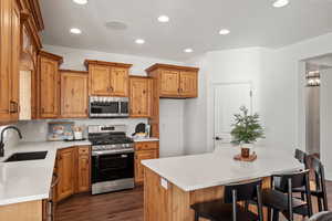 Kitchen with stainless steel appliances, a breakfast bar area, a center island, dark wood-style floors, and brown cabinets