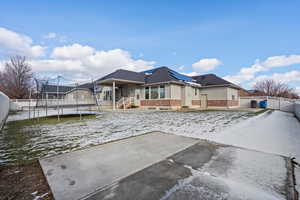 Rear view of house with a fenced backyard, a trampoline, a patio area, stucco siding, and brick siding