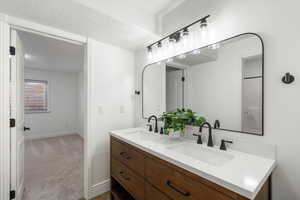 Bathroom featuring double vanity, dark colored carpet, and a textured ceiling
