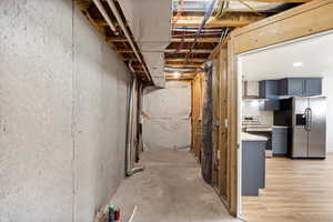 Unfinished basement featuring stainless steel refrigerator with ice dispenser