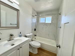 Bathroom featuring bathing tub / shower combination, vanity, light wood-style floors, a textured ceiling, and a textured wall