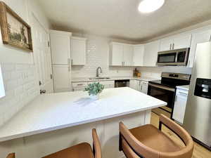 Kitchen with appliances with stainless steel finishes, a peninsula, light stone counters, a breakfast bar, and a textured ceiling