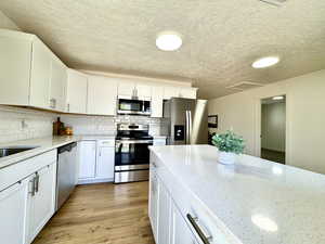 Kitchen with stainless steel appliances, white cabinetry, light stone countertops, a textured ceiling, and light wood-style floors